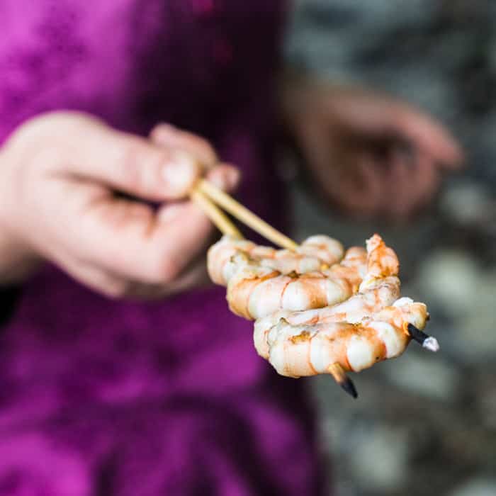 Woman in pink top holding out a wooden skewer of pink juicy king prawns