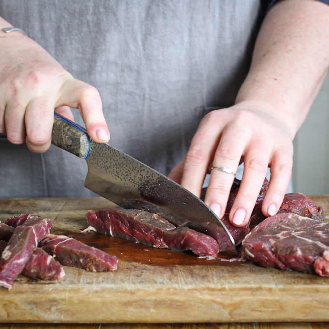 Woman slicing beef with a silver knife on a wooden board