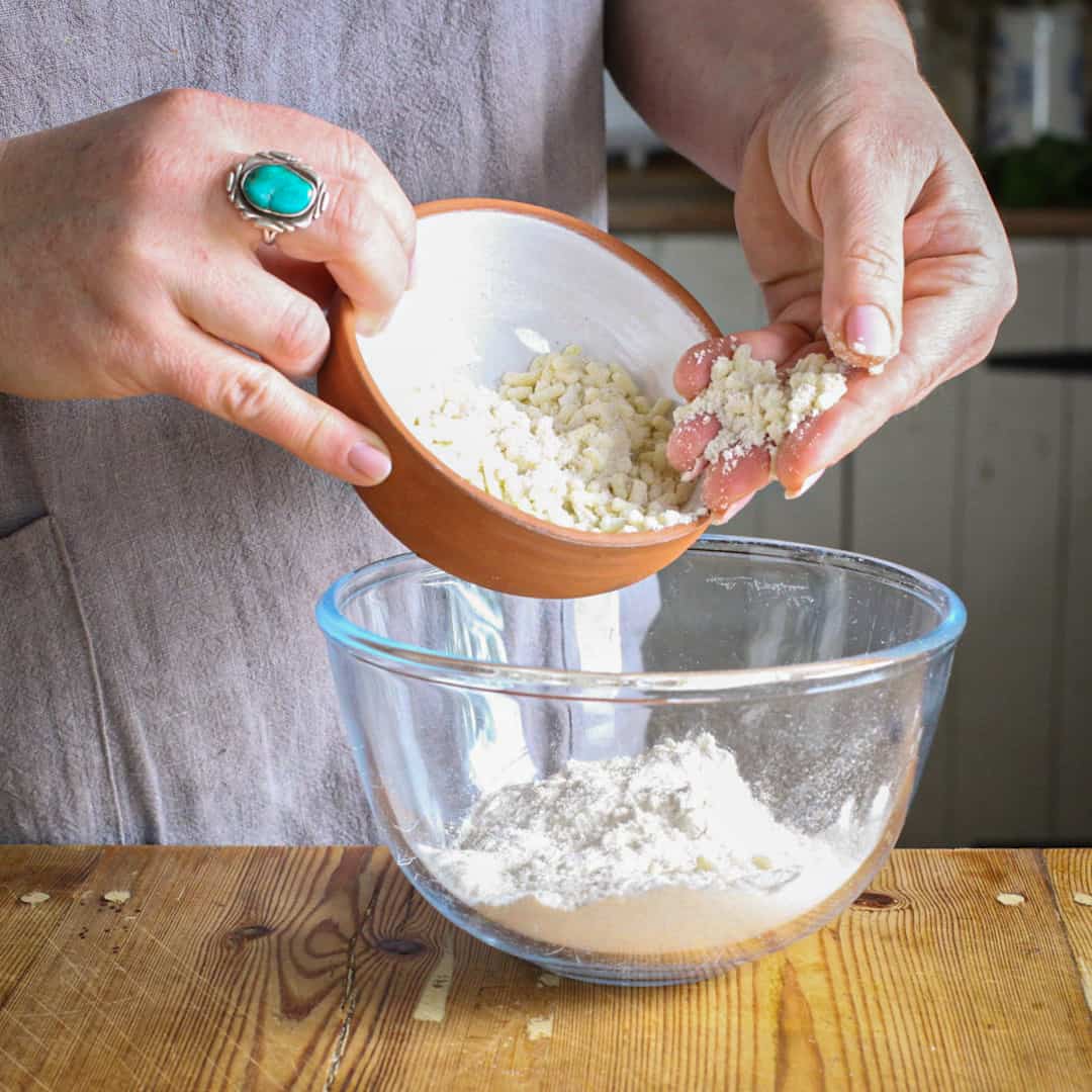 Womans hands tipping beef suet into a glass bowl of flour to make dumplings