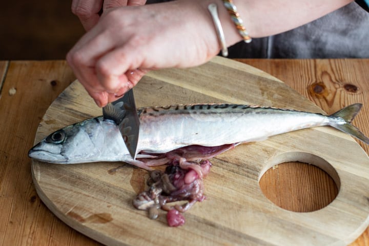 womans hands holiding a sharp silver knife and cutting the fin from a fresh makerel