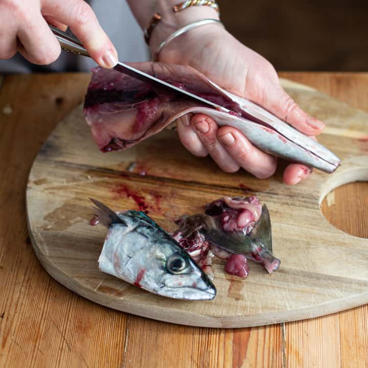 womans hands holding a mackerel and cutting it open to make sushi