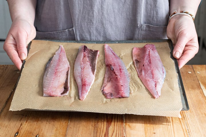 4 mackerel fillets on brown baking paper being held by a woman in a grey apron