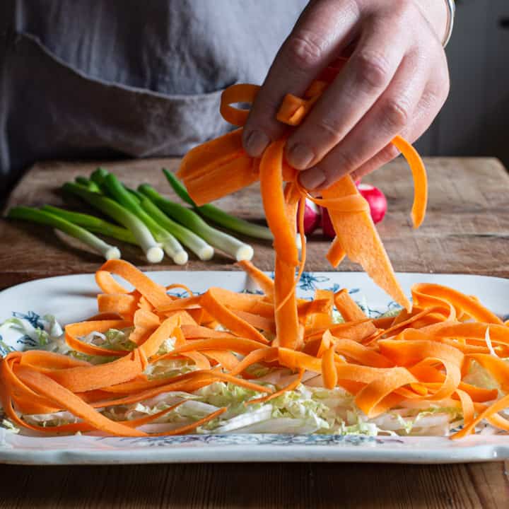 womans hand placing ribbon of peeled carrot onto a salad platter