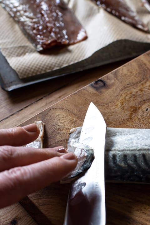 womans hands using a sharp silver knife to slice thin slices from a raw mackerel fillet