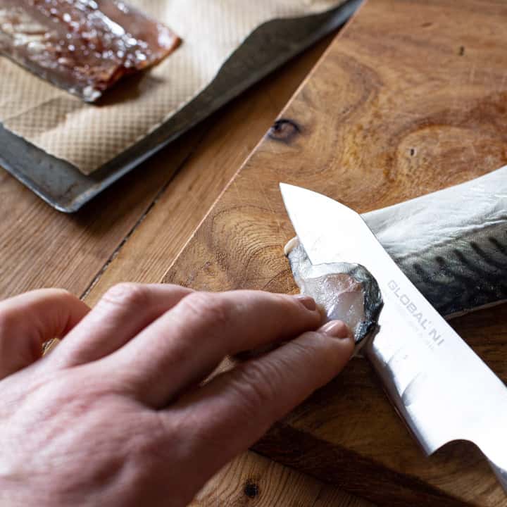 womans hands using a sharp silver knife to slice thin slices from a raw mackerel fillet