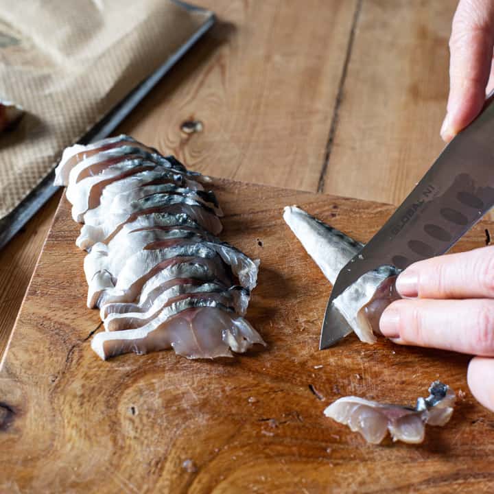 womans hands using a sharp silver knife to slice thin slices from a raw mackerel fillet