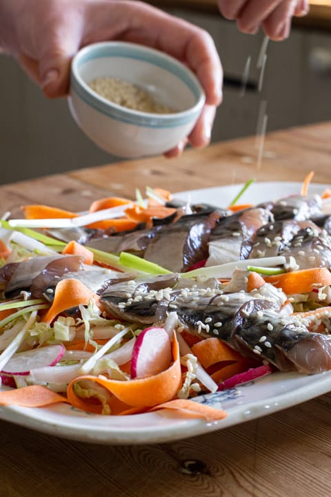 woman sprinkling sesame seeds onto a mackerel sashimi platter