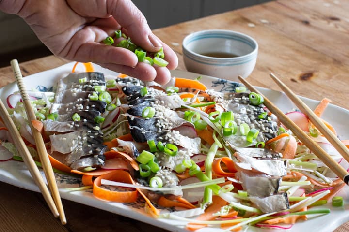 womands hands sprinkly chopped green onion onto a white plate of homemade sashimi salad