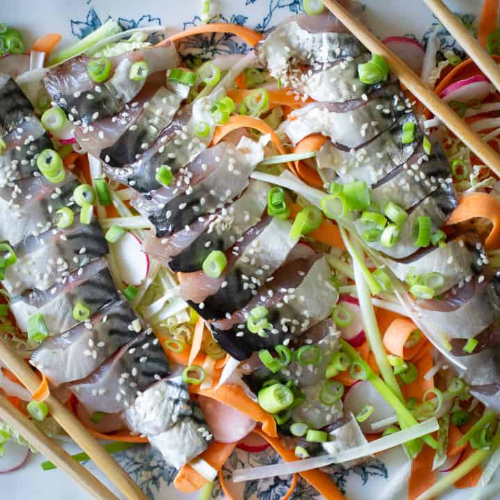 blue and white plate of raw fish sashimi salad, salad and chopsticks