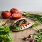 wooden board with fresh salads scattered around and a pitta bread stuffed with salad and two beef kofta kebabs