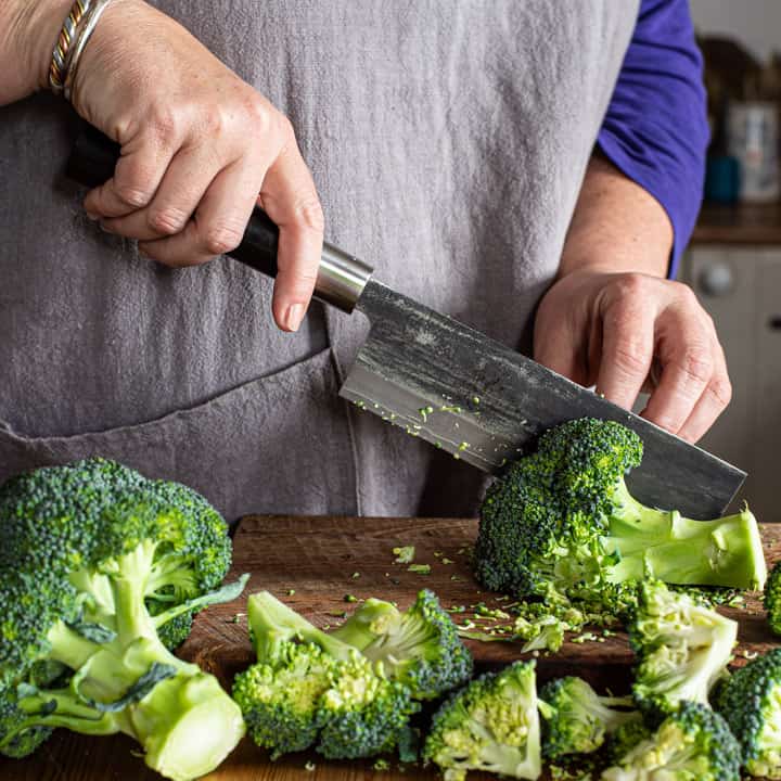 womans hands chopping fresh broccoli with Japanese knife on a wooden board