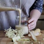 Woman in grey pouring a cream coloured smoothie into a glass jar