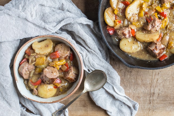 white bowl of hearty sausage and cider campfire skillet with a cast iron skillet in the background