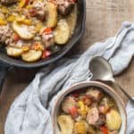 white bowl of hearty sausage and cider stew with a cast iron skillet in the background