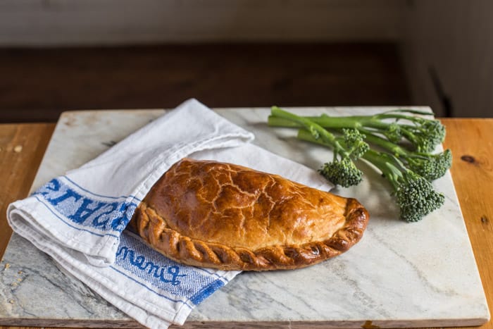 Tenderstem and Cornish Blue Cheese Pasty in a blue and white tea towel on a marble board with tenderstem along side