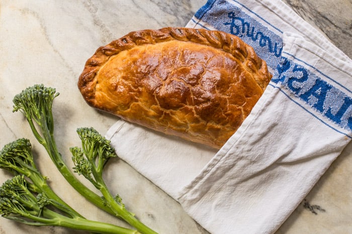 Tenderstem and Cornish Blue Cheese Pasty in a blue and white tea towel on a marble board with tenderstem along side