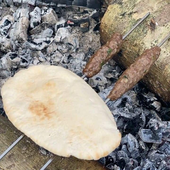 2 metal skewers with kebabs on resting over a fire with a pitta bread resting on the skewers toasting