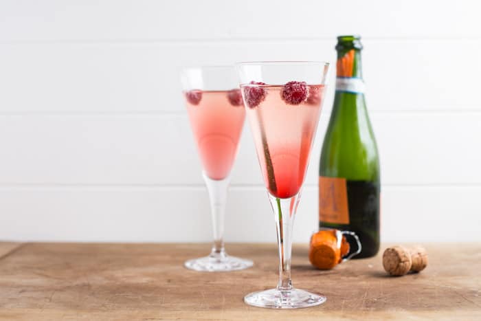 A bottle of Prosecco, 2 cocktail glasses with pink kir royale recipe in them and a cork