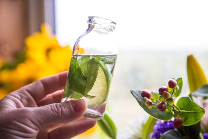 Mojito Fruit Salad Dressing held in a small glass bottle with flowers behind