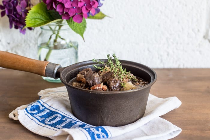 Slow Cooker Venison in Cider in a saucepan on a tea cloth with flowers beside