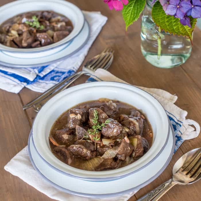 Slow Cooker Venison in Cider in blue and white bowls with spoons and forks on a table top