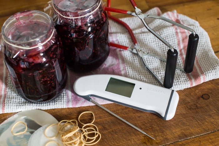 Sloe and blackberry hedgerow jam in jars on a kitchen table with jam making equipment