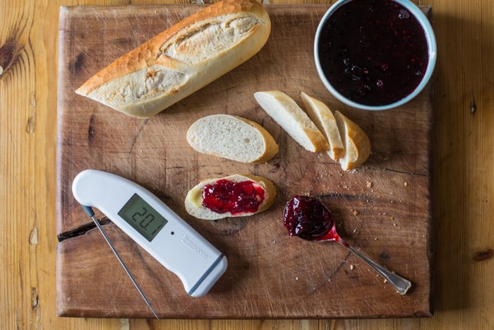 Sloe and blackberry hedgerow jam on crusty bread surrounded by more bread a bowl of jam and a spoon on a wooden table