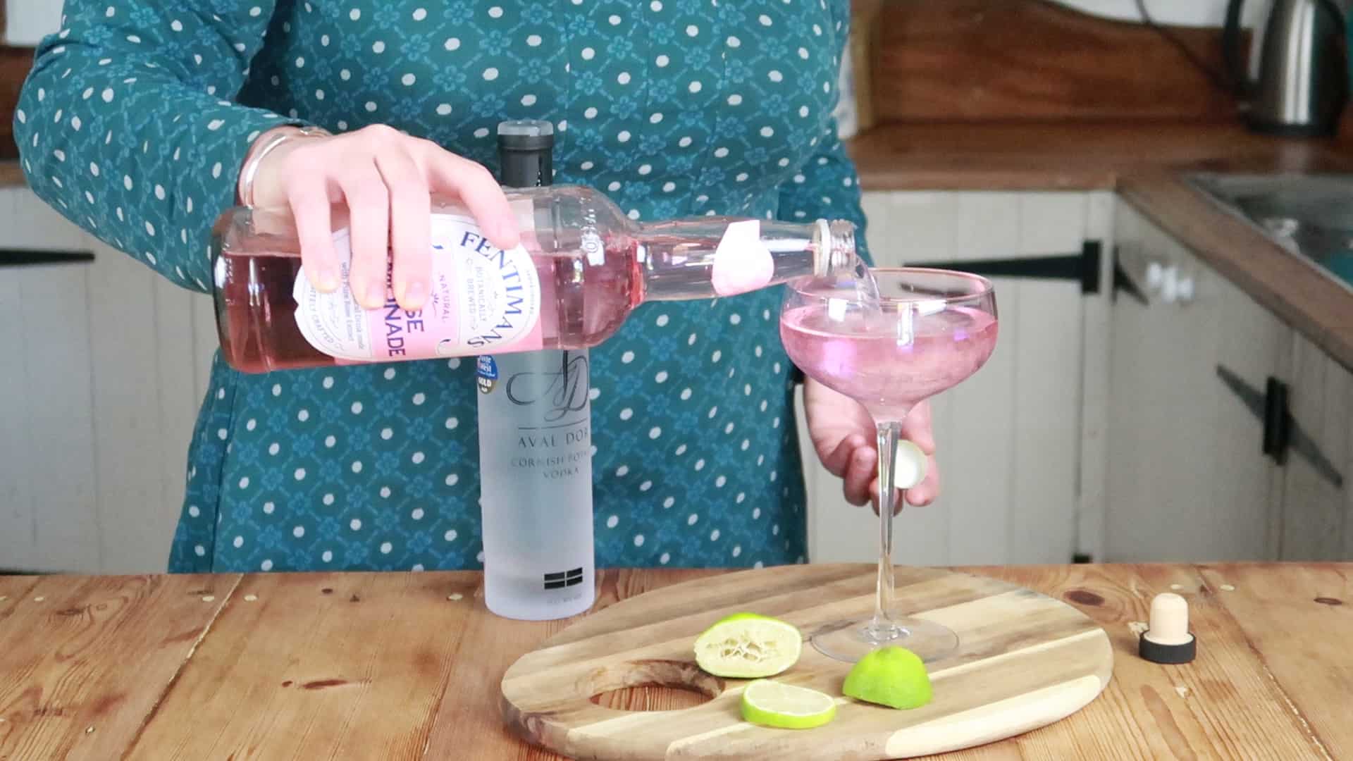 Person pouring lemonade into a cocktail glass stood on a wooden chopping board