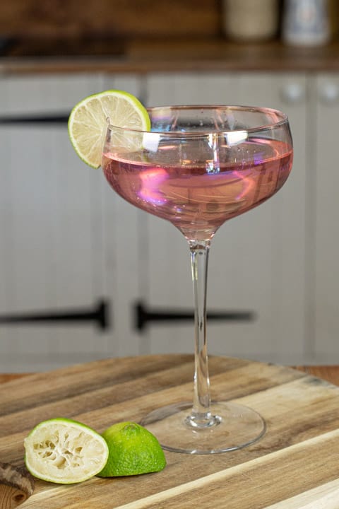 Glass containing pink cocktail on a wooden surface with a slice of lime