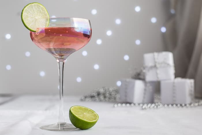 Glass of Pink Elephant Cocktail garnished with a slice of Lime and festive parcels on a grey and white background