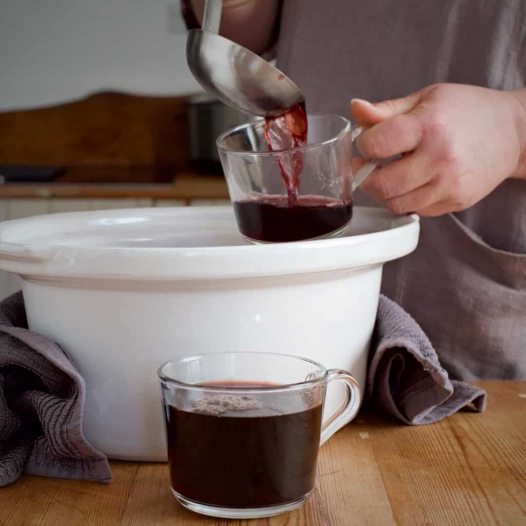 Woman ladling hot mulled wine from a white bowl into a glass mug with a silver spoon