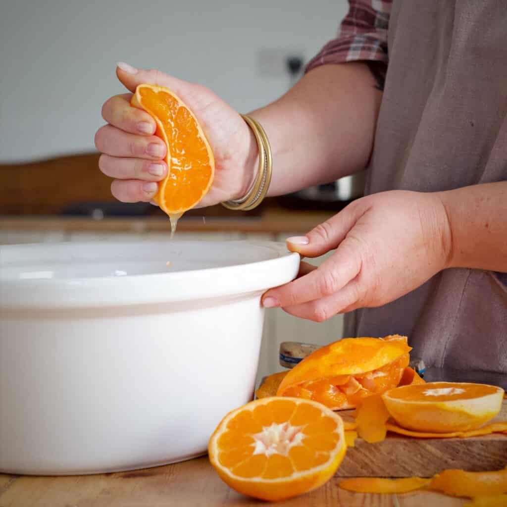 Womans hands squeezing juice from half a satsuma into a white slow cooker pot