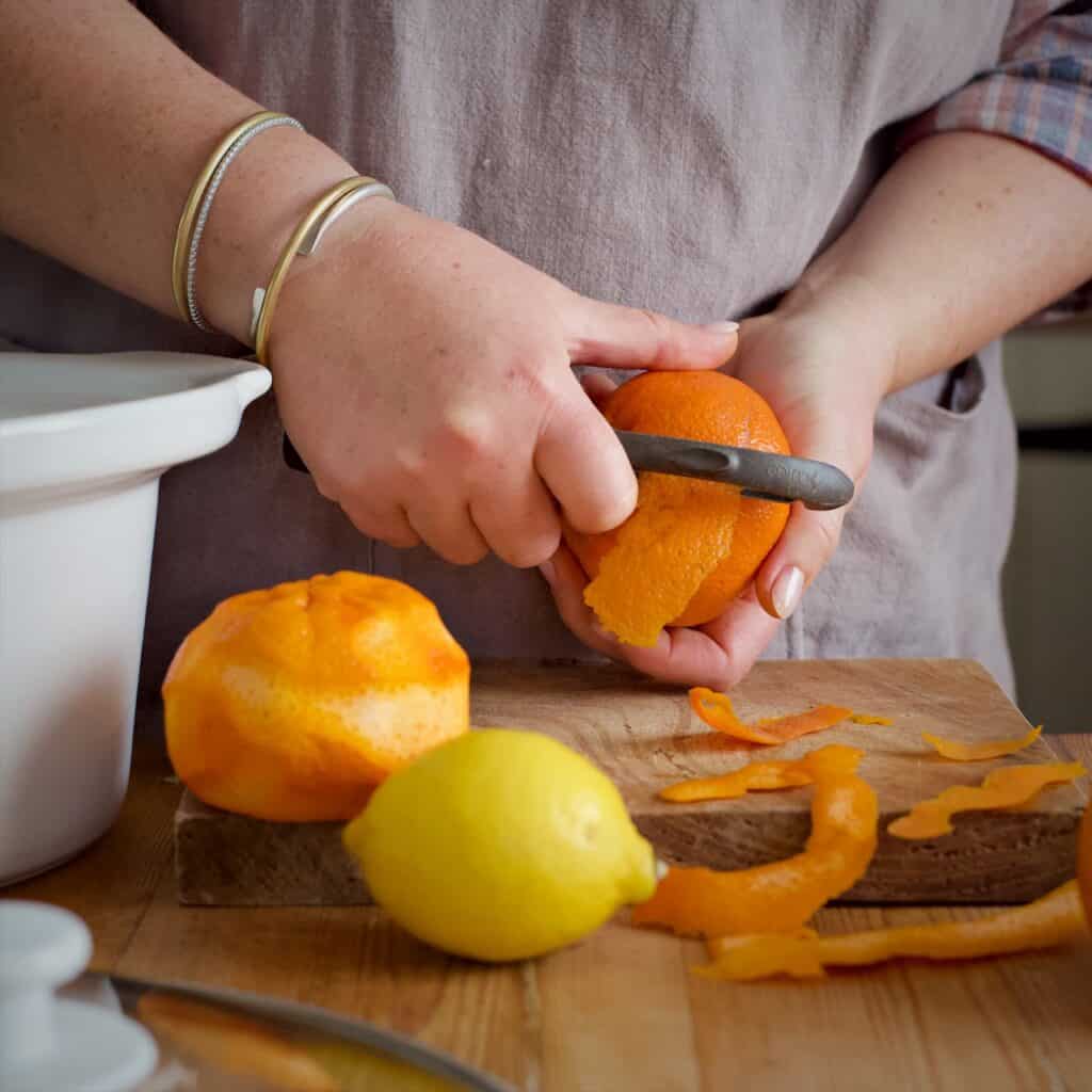 Woman in grey apron peeling satsumas over a wooden chopping board