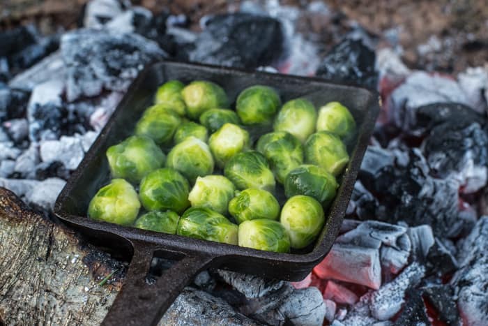 Brussels sprouts cooking on a campfire in a roasting tin for Festive Dirty Steak Salad