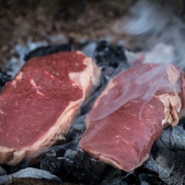 two dirty steaks cooking on the embers of a campfire