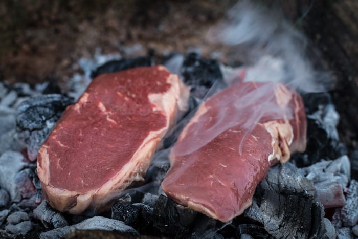 Festive Dirty Steak Salad -two dirty steaks cooking on the embers of a campfire