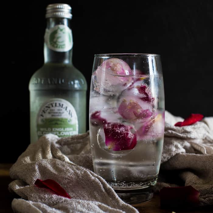 Rose and Elderflower Mocktailover ice in a tall glass with bottle of tonic and rose petals