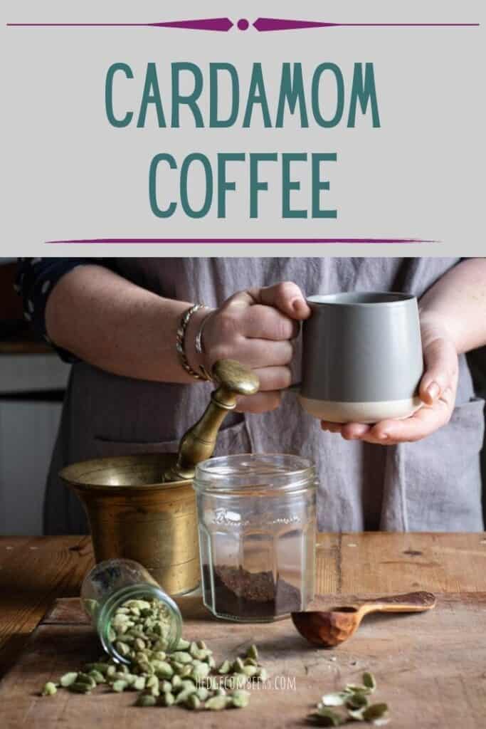 womands hands holding a grey mug of hot cardamom coffee over a messy scene of cardamom pods and coffee making paraphenalia