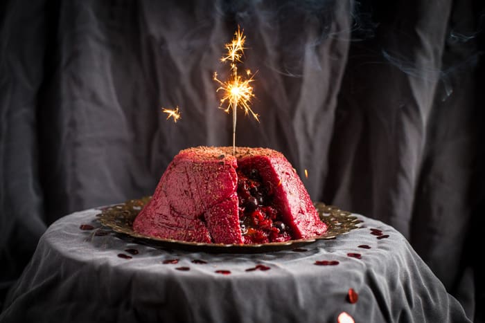 Wintry Summer Pudding on a silver plate with a sparkler on top on a grey cloth with scattered rose petels