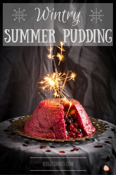 Wintry Summer Pudding on a silver plate with a sparkler on top on a grey cloth with scattered rose petals