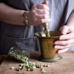 womans hands smashing green cardamom seeds in a brass pestle and mortar to make cardamom coffee