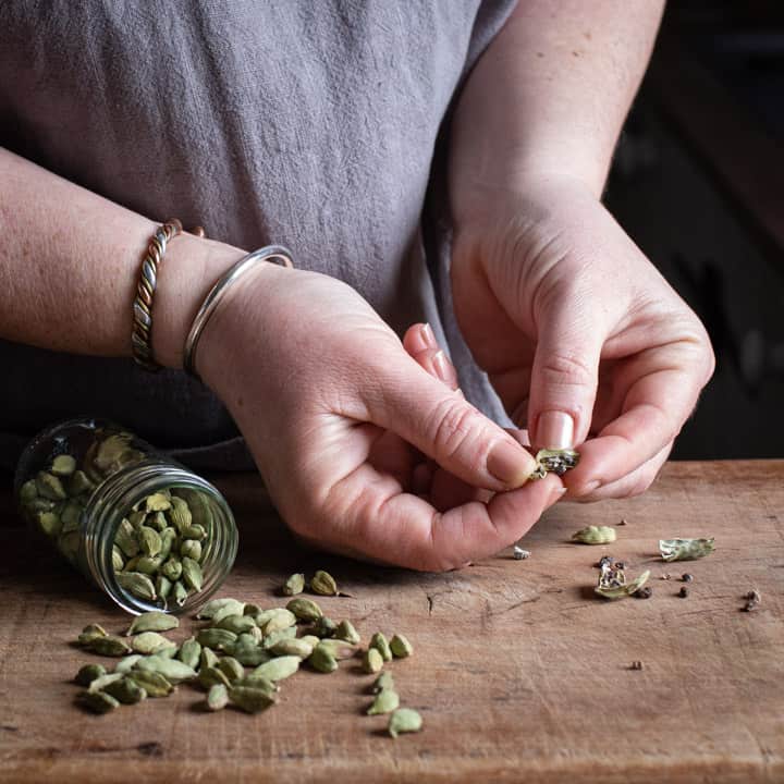 womans hands breaking apart green cardamom pods to remove the seeds for grinding