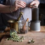 womans hands tipping freshly ground cardamom seeds into an Aeropress coffee maker
