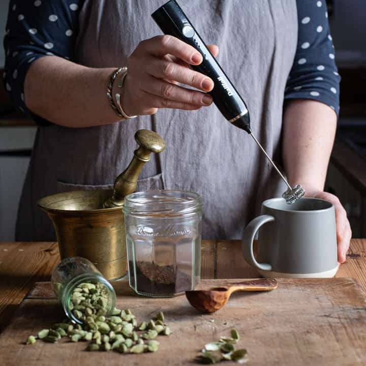 womans hands plunging a milk frother into a grey mug of coffee