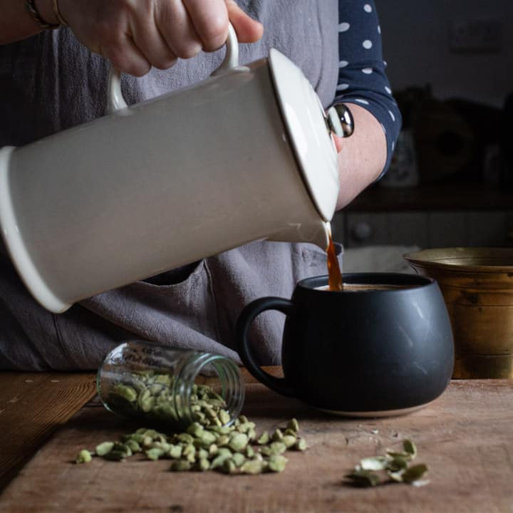 womans hands pouring hot coffee into a black mug form a white coffee pot