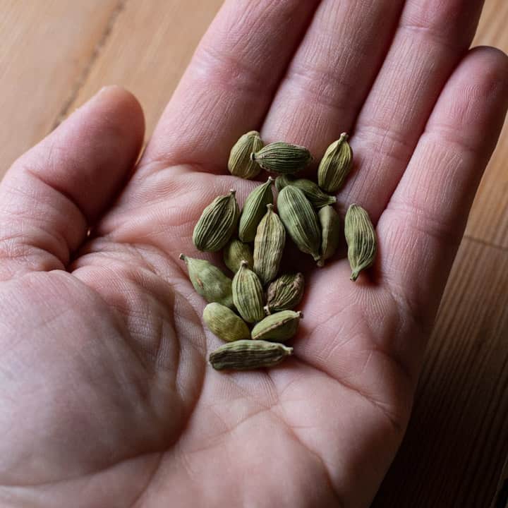 womans hand holding green cardamom pods