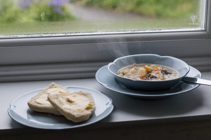 Traditional Shetland Reestit Mutton Stew a white bowl on a window ledge beside a plate with a buttered bannock