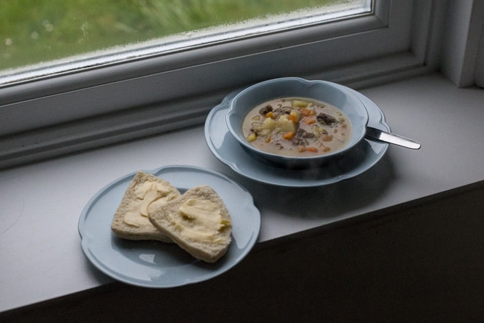 Traditional Shetland Reestit Mutton Stew a white bowl on a window ledge beside a plate with a buttered bannock