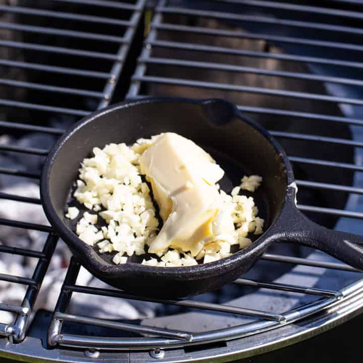 small black skillet of butter and raw garlic on a BBQ grill about to be cooked