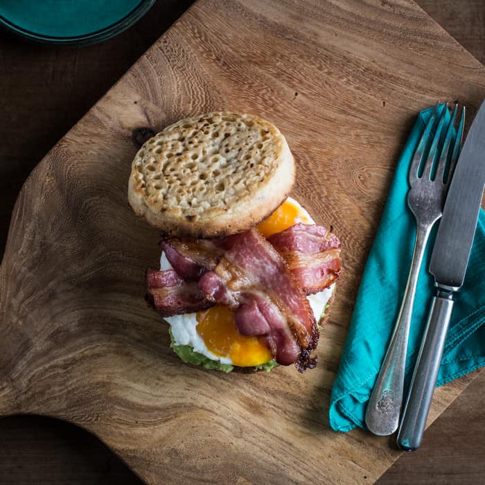 Breakfast Crumpet Burger on a wooden board with a knife and fork and a cup of coffee